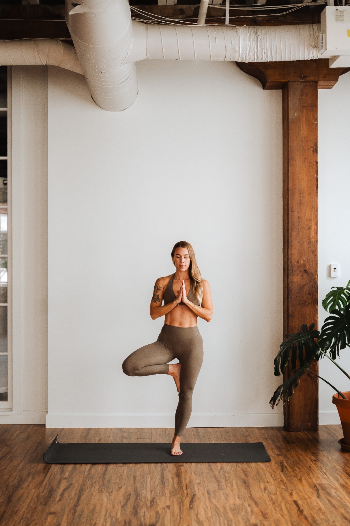 Kelli Blake in tree pose on a mat in a warm loft studio