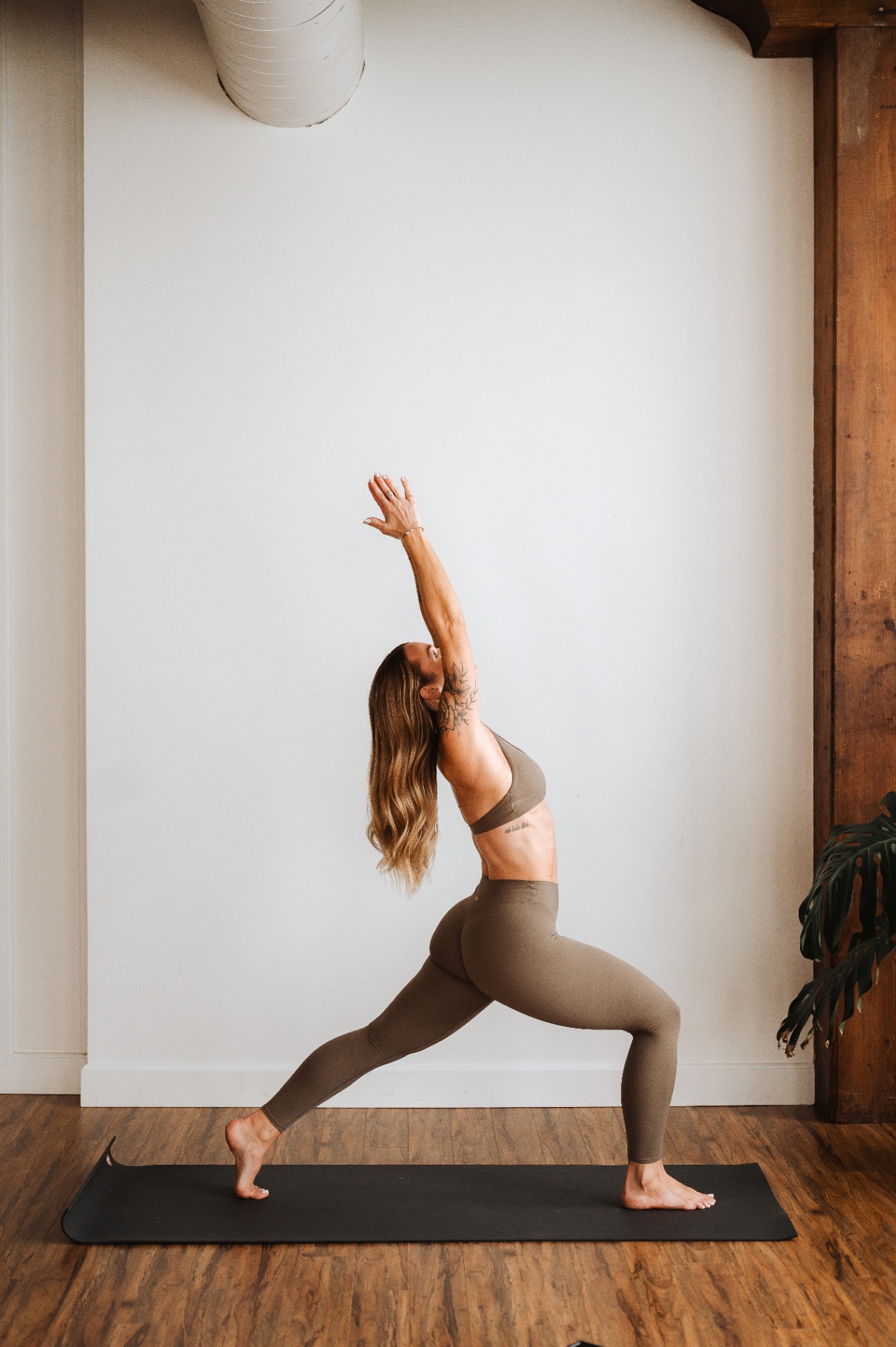 Kelli Blake in a warrior pose on a mat in a loft studio