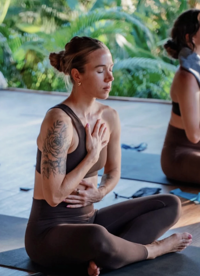 A woman seated in quiet meditation on a retreat deck surrounded by tropical greenery